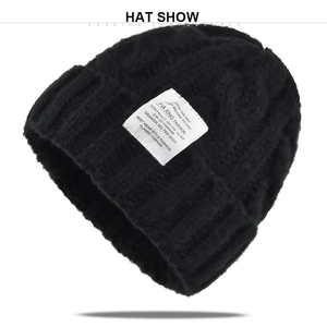 Detailed view of black cable knit beanie featuring industrial style white cloth label