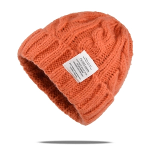 Close-up of orange cable knit beanie with cuffed edge and white woven brand label