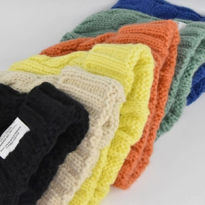 Close-up showing a variety of colorful cable knit beanies with ribbed cuffs and labels