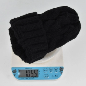 Detail showing the weight of the black cable-knit beanie on a digital scale at 105.5g