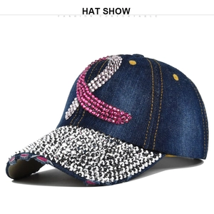 Close-up of denim baseball cap featuring pink rhinestone ribbon and distressed brim detail