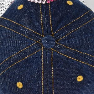 Detailed top view of denim baseball cap with gold contrast stitching and rhinestone accents