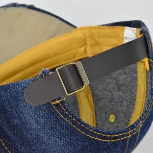 Detail of adjustable leather strap and bronze buckle on denim baseball cap
