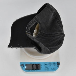 Close-up of a distressed grey cotton baseball cap showing frayed edge details on weighing scale