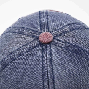 Close-up of washed denim fabric texture and top button detail on vintage baseball cap
