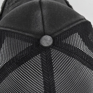 Detail view of black trucker hat featuring distressed cotton fabric and breathable mesh top