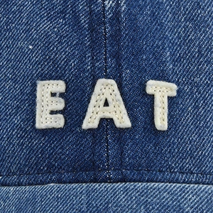 Close-up of deep blue denim baseball cap crown featuring white EAT felt embroidery