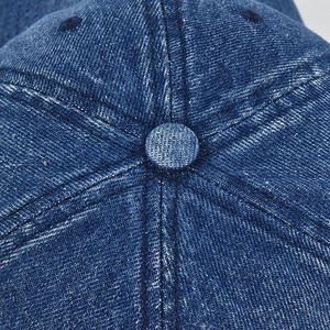Macro shot of top button and stitching details on a washed blue denim baseball cap