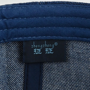 Detail of blue washed denim cap showing woven brand label and precise stitching texture