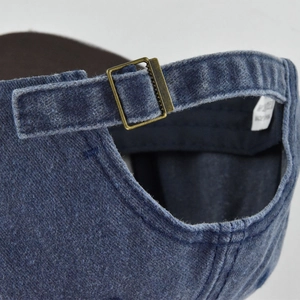 Detail of adjustable brass buckle and strap on blue washed denim baseball cap