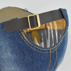 Détail de la sangle réglable en cuir et boucle dorée sur une casquette en jean bleue