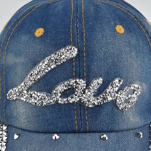 Detailed view of silver rhinestone Love art lettering and studs on blue denim baseball cap