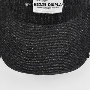 Detail view of black denim baseball cap showing vintage distressed brim and woven patch