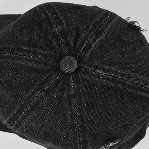 Macro view of distressed black denim baseball cap showing fabric texture and crown detail
