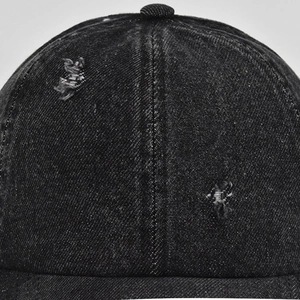 Close-up of distressed denim texture on black baseball cap showing ripped details
