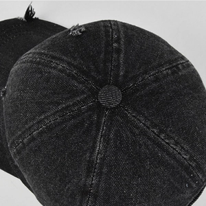 Macro shot of 6-panel stitched crown and fabric button on distressed black denim baseball cap