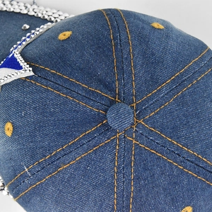 Detail of blue denim baseball cap with yellow stitching and sparkling silver rhinestones