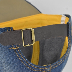 Blue denim baseball cap back detail with brown leather strap and brass metal buckle