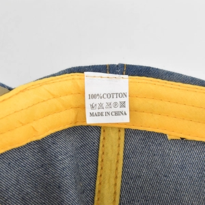 Detail view of denim baseball cap interior showing yellow sweatband and 100% cotton label