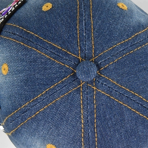 Macro view of denim baseball cap crown showing yellow stitching and star embroidery