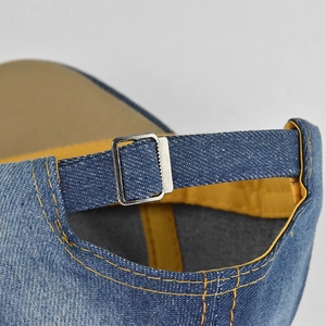 Detail of adjustable silver metal buckle and yellow stitching on blue denim baseball cap