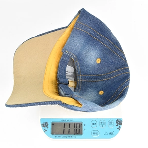 Detailed top view of denim baseball cap on scale weighing 111 grams with metal buckle