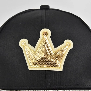 Macro view of a black baseball cap featuring a golden sequin crown patch and rhinestones