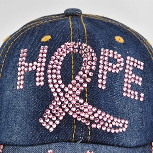 Gros plan détaillé des strass roses formant HOPE sur une casquette en jean bleu foncé