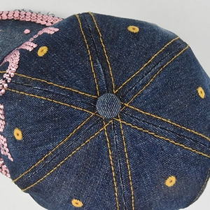 Gros plan sur casquette en jean avec coutures jaunes et détails en paillettes roses