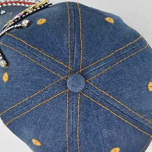 Dettaglio del berretto da baseball in denim blu scuro con cuciture gialle e strass