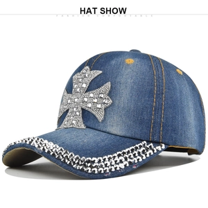Close-up of blue denim baseball cap featuring a large rhinestone cross and orange stitching