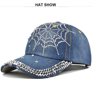 Close-up of a blue denim baseball cap featuring silver rhinestone spider web and metal studs