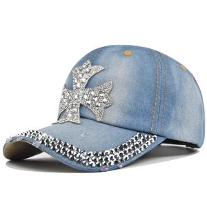 Detailed view of light blue denim baseball cap with rhinestone cross and studded brim detail