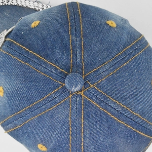 Detail of blue denim baseball cap showing contrast yellow stitching and embroidered eyelets