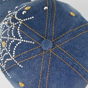 Macro detail of rhinestone patterns and contrast orange stitching on blue denim cap