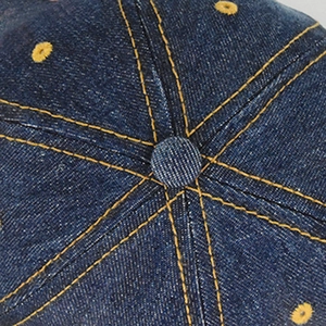 Macro shot of dark blue denim baseball cap crown with yellow contrast stitching details