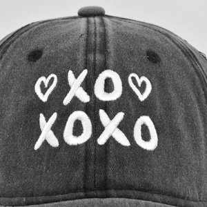 Front view of a dark gray washed denim baseball cap with white 3D XOXO heart embroidery