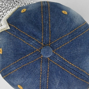 Détail de la casquette en denim bleu avec surpiqûres jaunes et patch étoile étincelant
