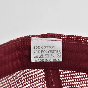 Macro shot of product care label inside a burgundy mesh cap showing 80% cotton blend fabric
