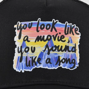 Détail d'une casquette noire avec écusson paysage de montagne au coucher du soleil et texte