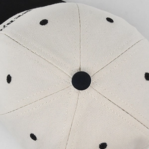 Detailansicht einer cremefarbenen Baseballkappe mit schwarzen Punkten und Twill-Gewebe