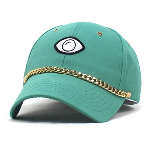 Detail of teal baseball cap with golden chain and large eye embroidery on front