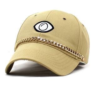 Close-up of beige baseball cap with eyeball embroidery and a thick gold metal chain