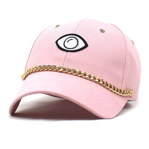 Close-up of pink baseball cap featuring eye embroidery and chunky gold metal chain detail