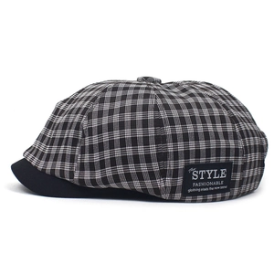 Detail of plaid newsboy cap showing black brim and stitched decorative side label