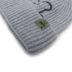 Detail of light grey ribbed knit beanie showing green woven label with smile icon