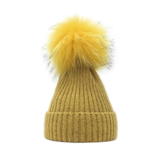 Detailed texture of mustard yellow knit beanie with a fluffy faux fur pom-pom on top