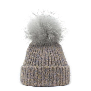 Detailed knit texture and fluffy raccoon fur pom-pom on purple-grey winter beanie