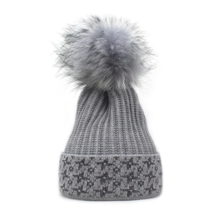 Dettaglio del berretto in maglia grigia con pompon soffice e motivi a stelle glitterate