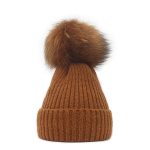 Detailed close-up of brown knit beanie showing soft fur pompom and ribbed texture